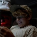 a young boy sitting in a chair looking at a cell phone